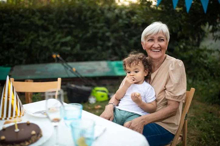 une grand mère qui fête son anniversaire avec son petit fils dans les bras